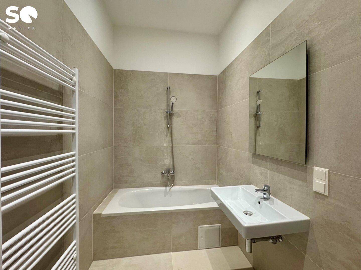 Modernes Badezimmer mit beigefarbenen Fliesen, Badewanne und beheiztem Handtuchhalter.