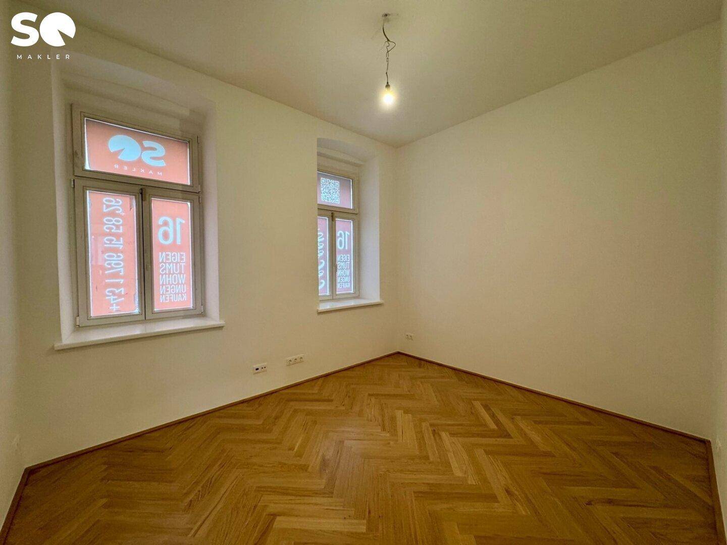 Helles Schlafzimmer mit zwei Fenstern und elegantem Fischgrätparkettboden.