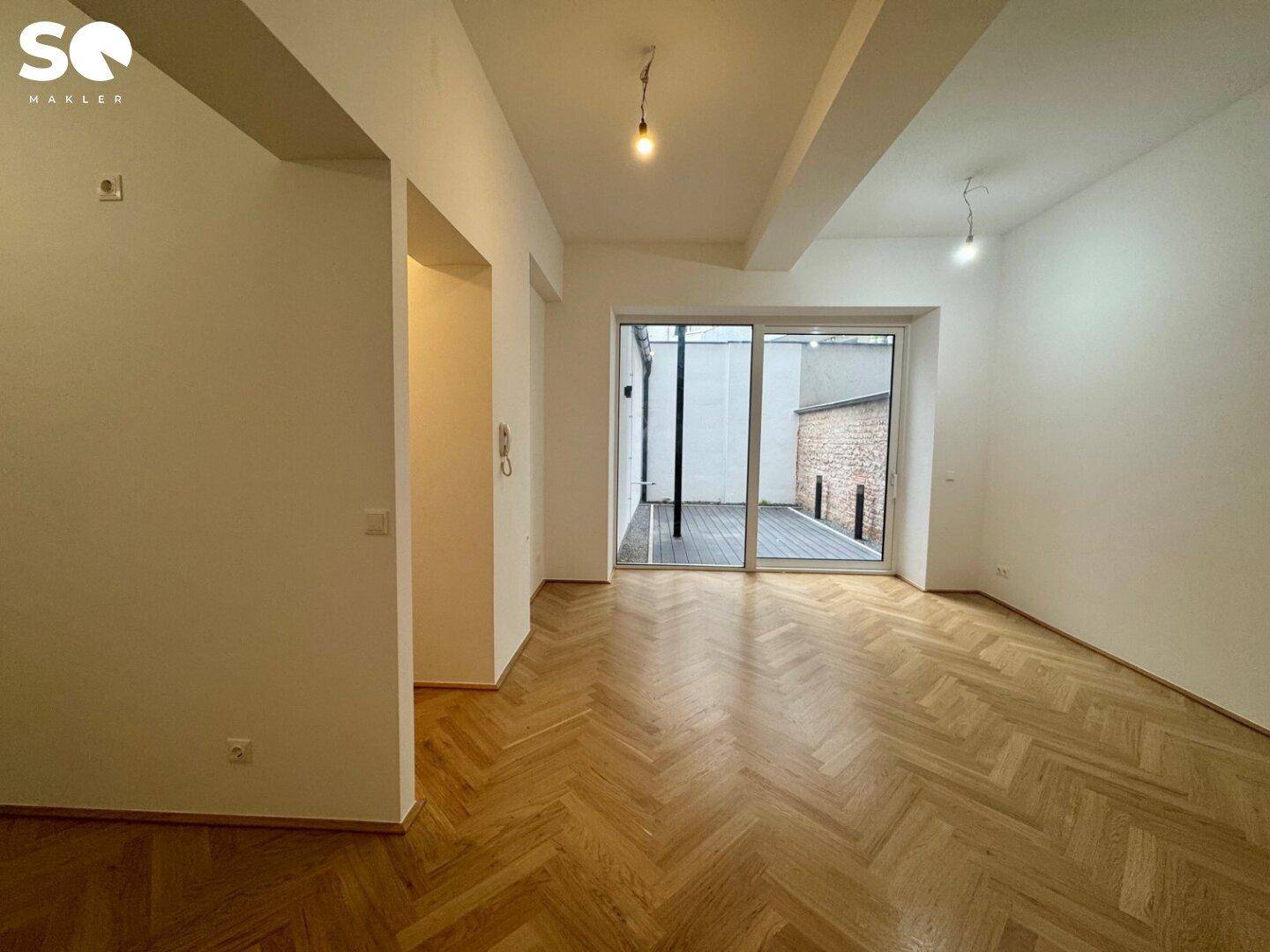 Geräumiger Wohnbereich mit Fischgrätparkett und direktem Zugang zur privaten Terrasse.