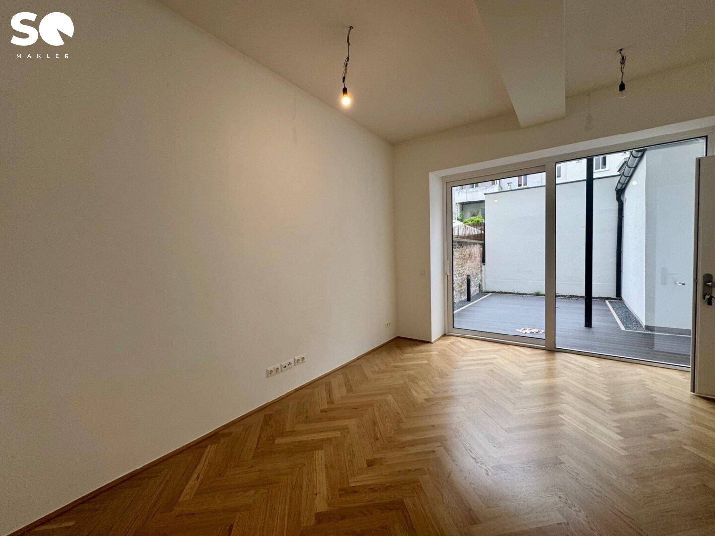 Heller Wohnraum mit elegantem Fischgrätparkett und direktem Zugang zu einer privaten Terrasse.