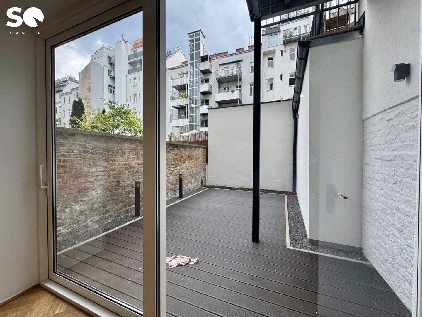 Innenansicht eines Raumes mit großem Schiebefenster, das Zugang zur modernen Außenterrasse bietet.