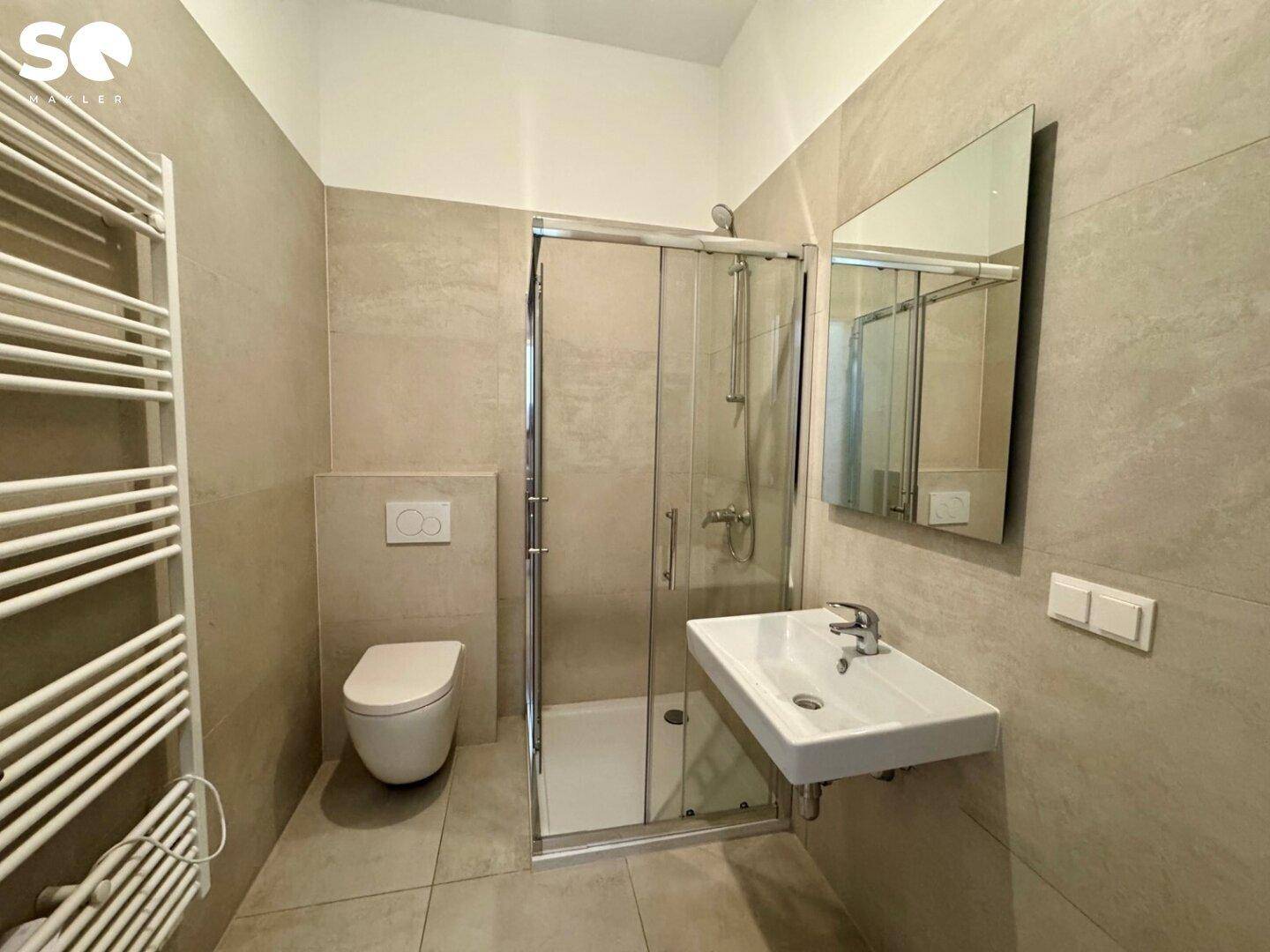 Modernes Badezimmer mit beigefarbenen Fliesen, wandhängendem WC, ebenerdiger Dusche und Handtuchheizkörper.