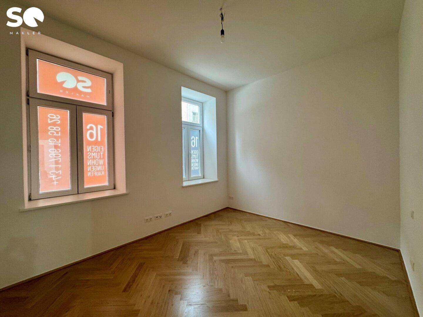 Helles Zimmer mit elegantem Fischgrätparkett und zwei Fenstern, ideal als Schlaf- oder Arbeitszimmer.