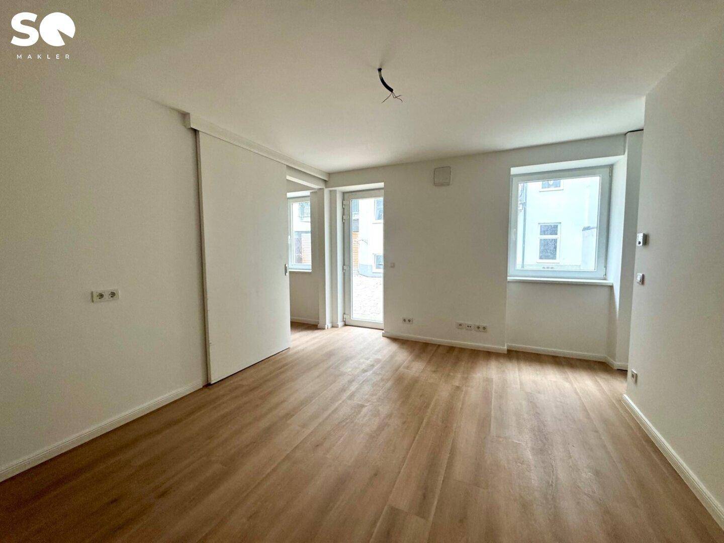 Geräumiger, heller Raum mit Laminatboden und Zugang zu einem Außenbereich.