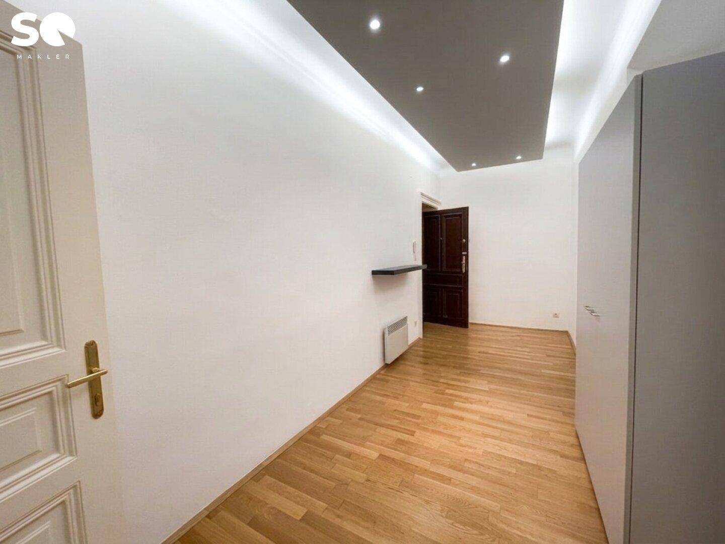 Flur mit Holzparkettboden, moderner Deckenbeleuchtung und einem Einbauschrank am Ende des Raumes.