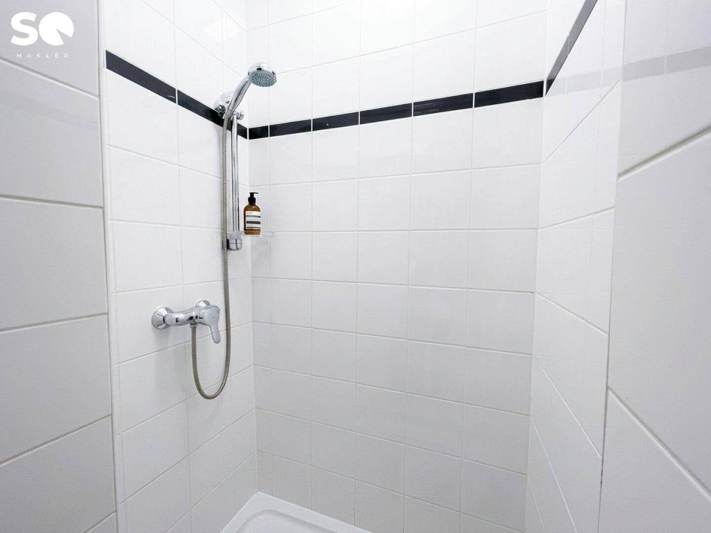 Modern geflieste Duschkabine mit weiß-schwarzem Fliesendesign und einer Handbrause.