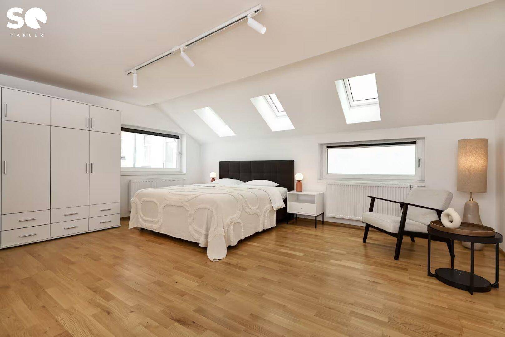 Helles Schlafzimmer im Dachgeschoss mit mehreren Dachfenstern, Holzboden und großem Kleiderschrank.