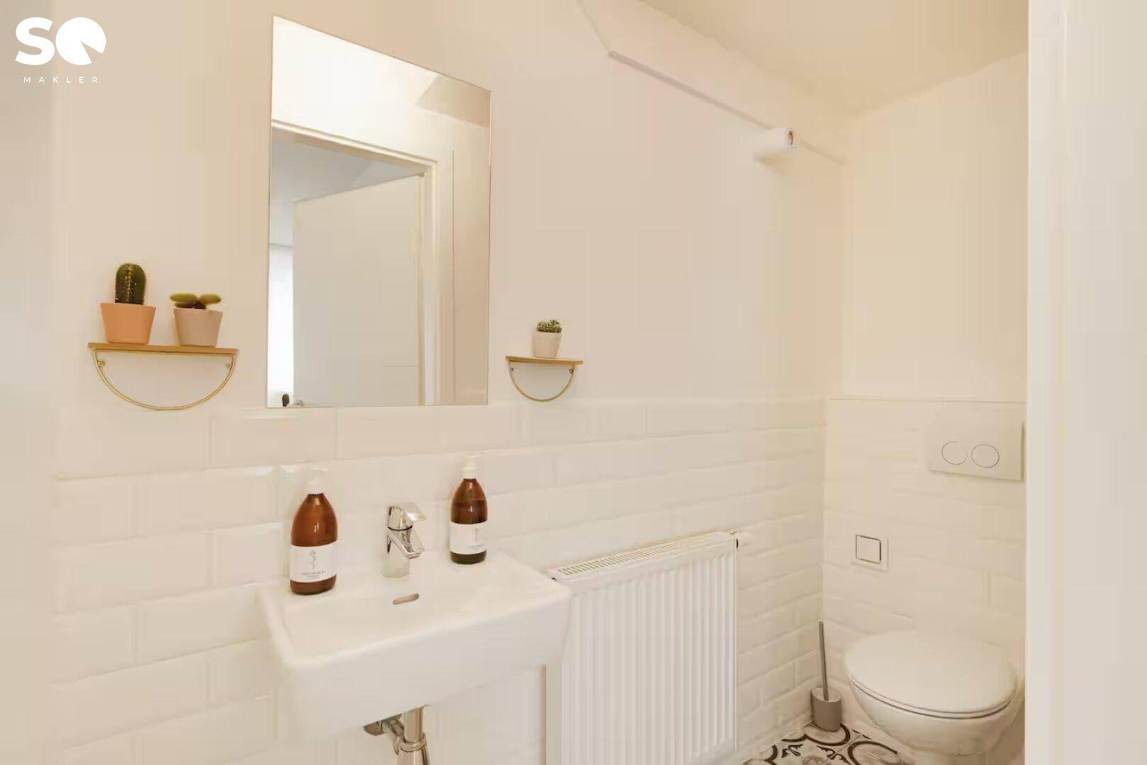 Modernes Gäste-WC mit weißen Fliesen, kleinem Waschbecken und dekorativen Bodenfliesen.
