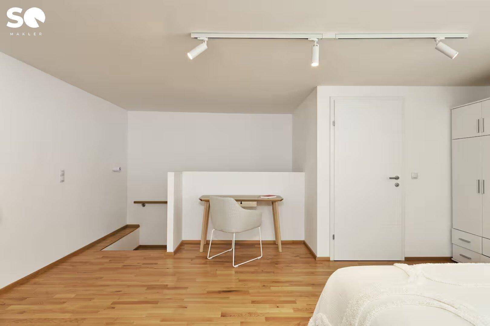 Heller Arbeitsbereich mit Schreibtisch, Kleiderschrank und Zugang zu einer unteren Ebene.