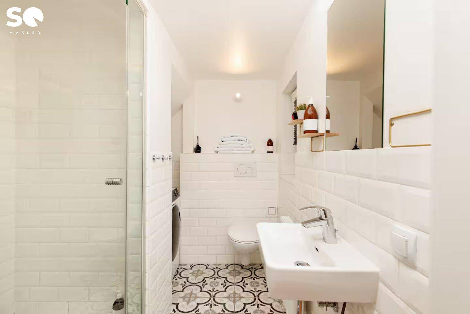Modernes Badezimmer mit Dusche, WC, Waschbecken und gemusterten Bodenfliesen.