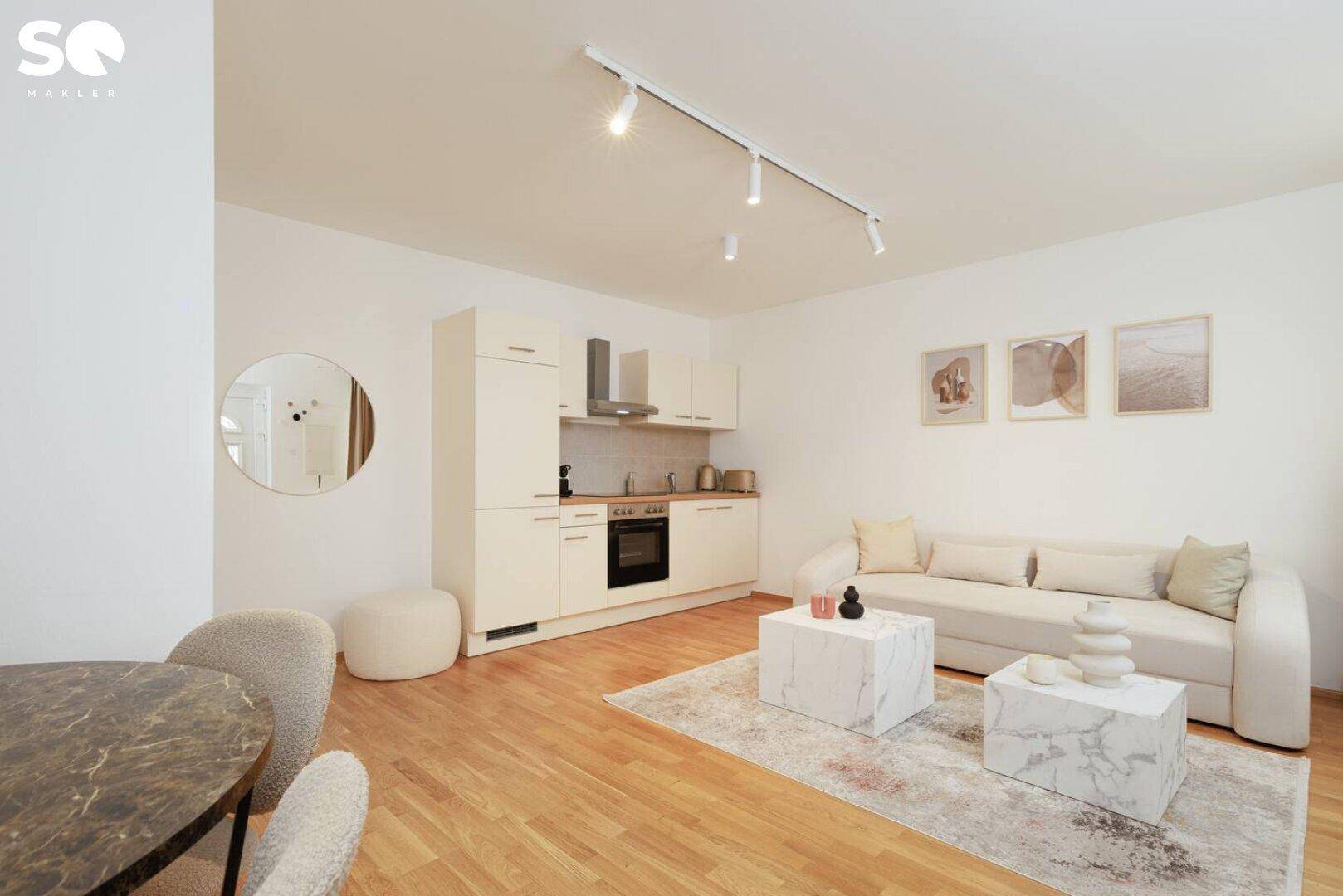 Gemütlicher Wohnbereich mit Sofa, Couchtischen und integrierter Küchenzeile in hellem Design.