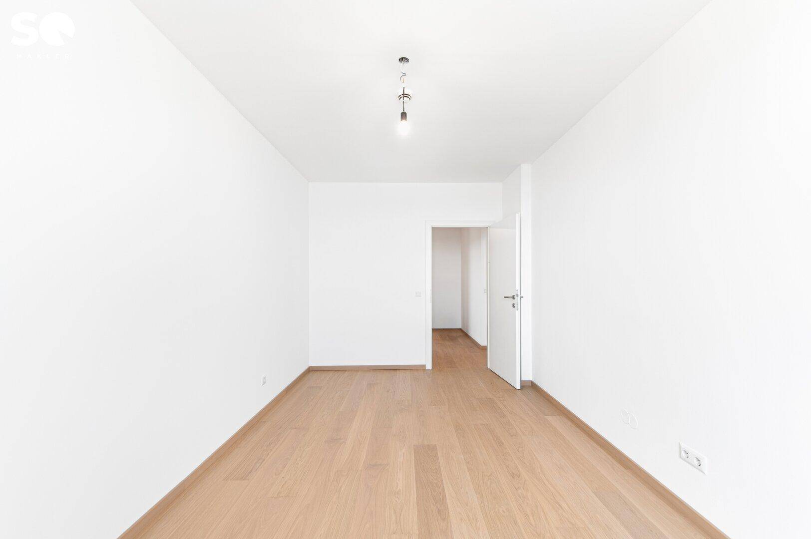 Leeres Schlafzimmer mit Parkettboden und Zugang zu einem weiteren Raum.