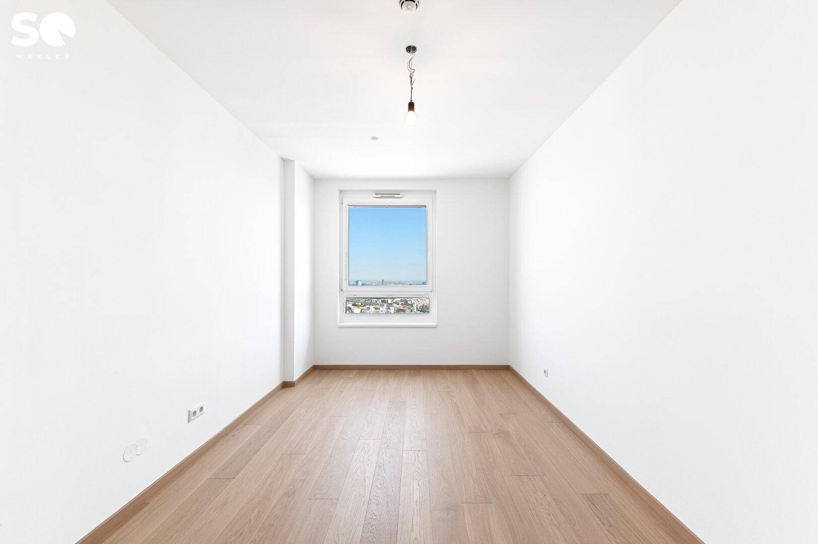 Helles Schlafzimmer mit Parkettboden und weitem Blick aus dem Fenster.