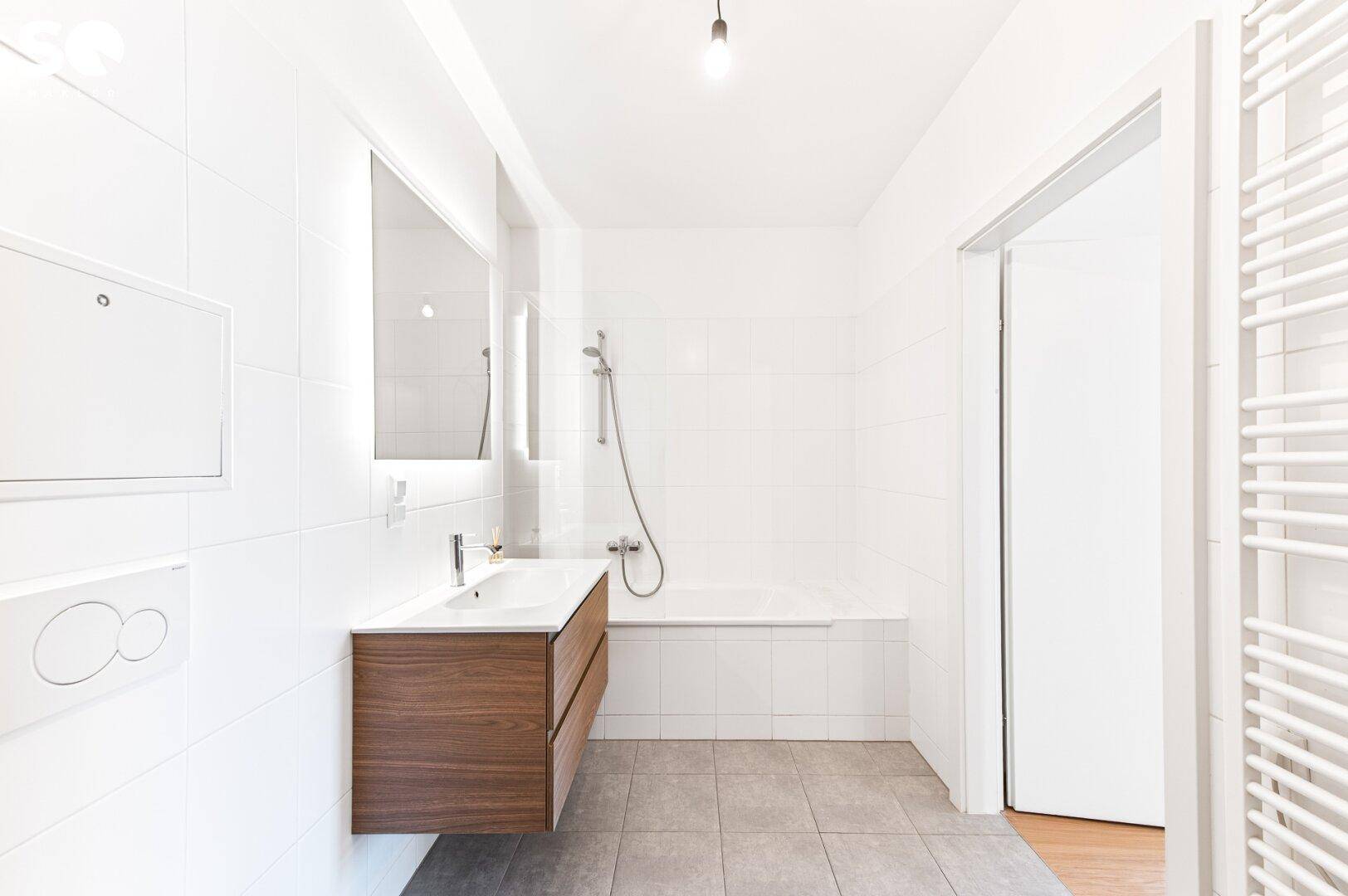 Modernes Badezimmer mit Badewanne, Holzwaschtisch und weiß gefliesten Wänden.