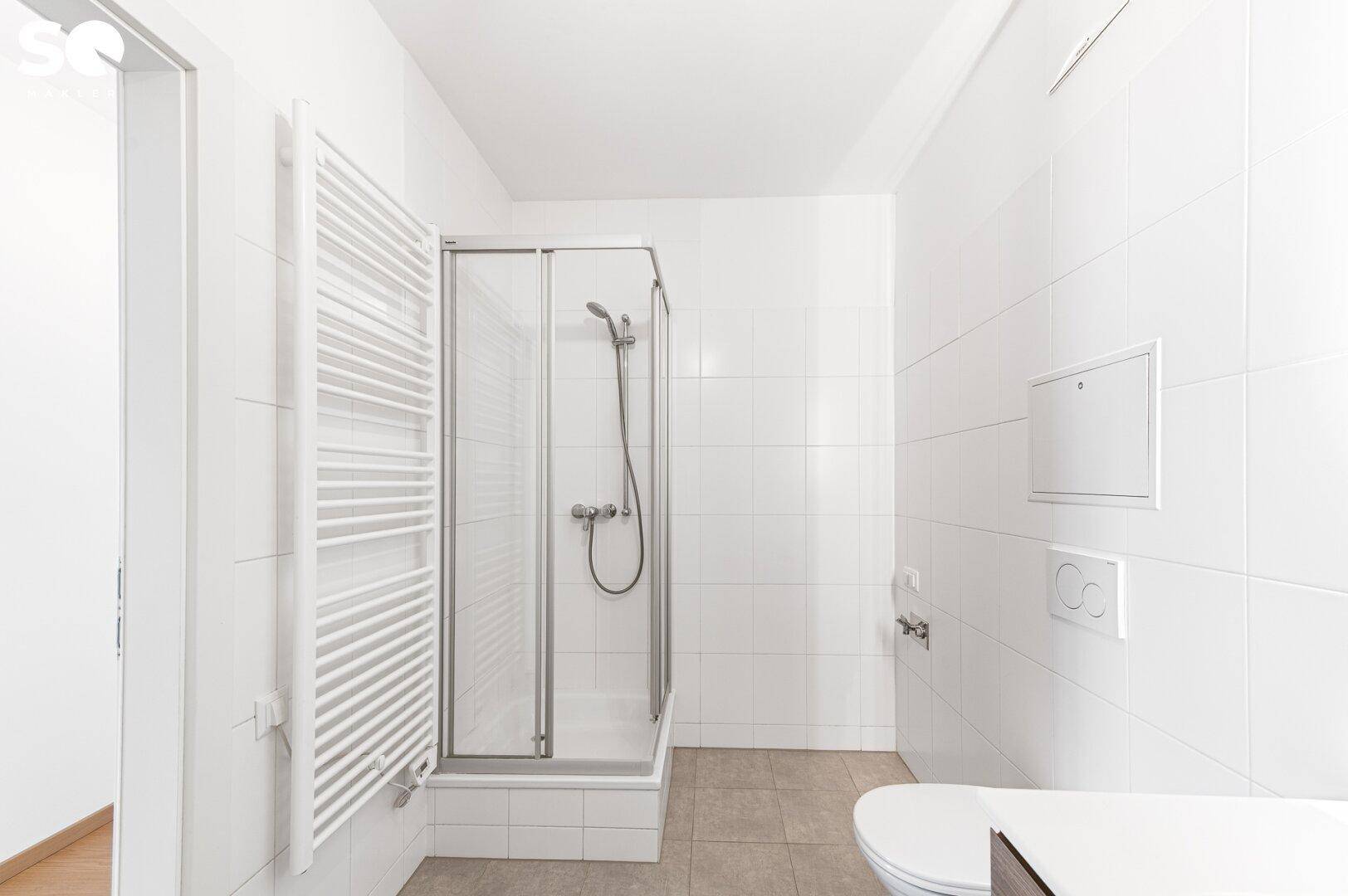 Badezimmer mit Duschkabine, Wand-WC und beheiztem Handtuchhalter.