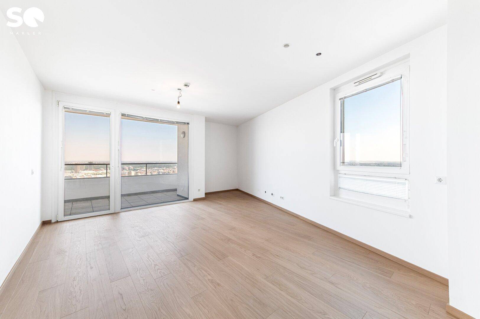 Heller Wohnbereich mit Holzparkettboden und Zugang zum Balkon mit Stadtblick.