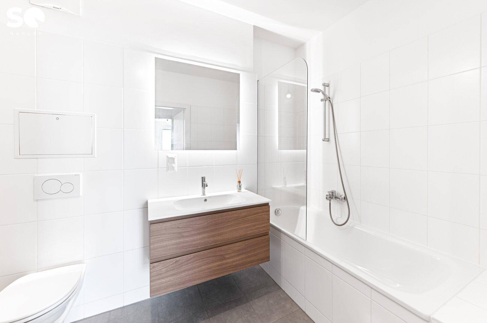Modernes Badezimmer mit weißen Fliesen, schwebendem Holzwaschtisch, Badewanne und Toilette.