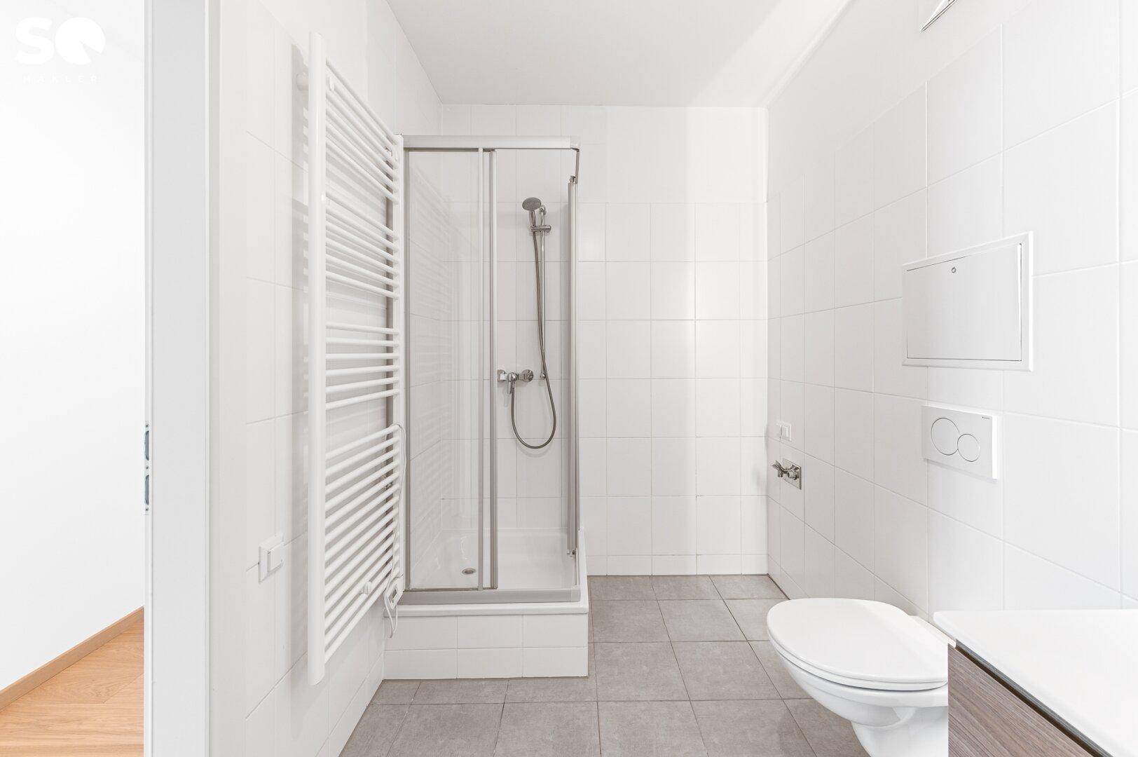 Modernes Badezimmer mit weißen Fliesen, Duschkabine, Toilette und einem beheizten Handtuchhalter.