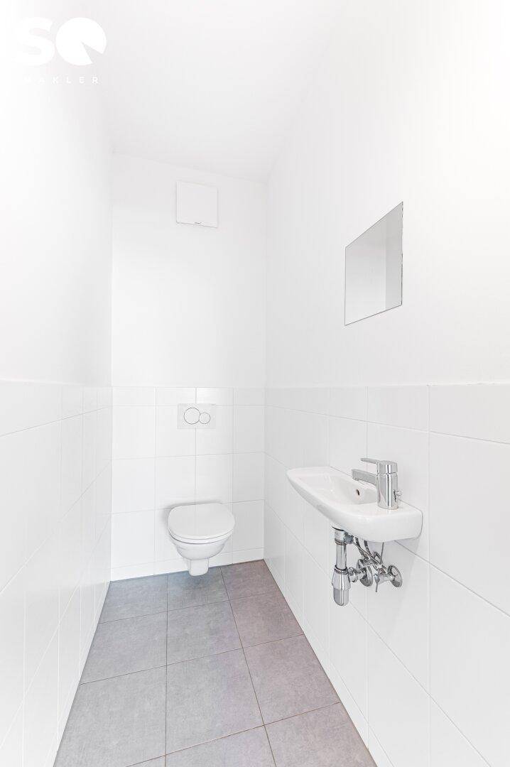 Kleines, helles Gäste-WC mit weißen Fliesen, wandhängender Toilette und einem Waschbecken.