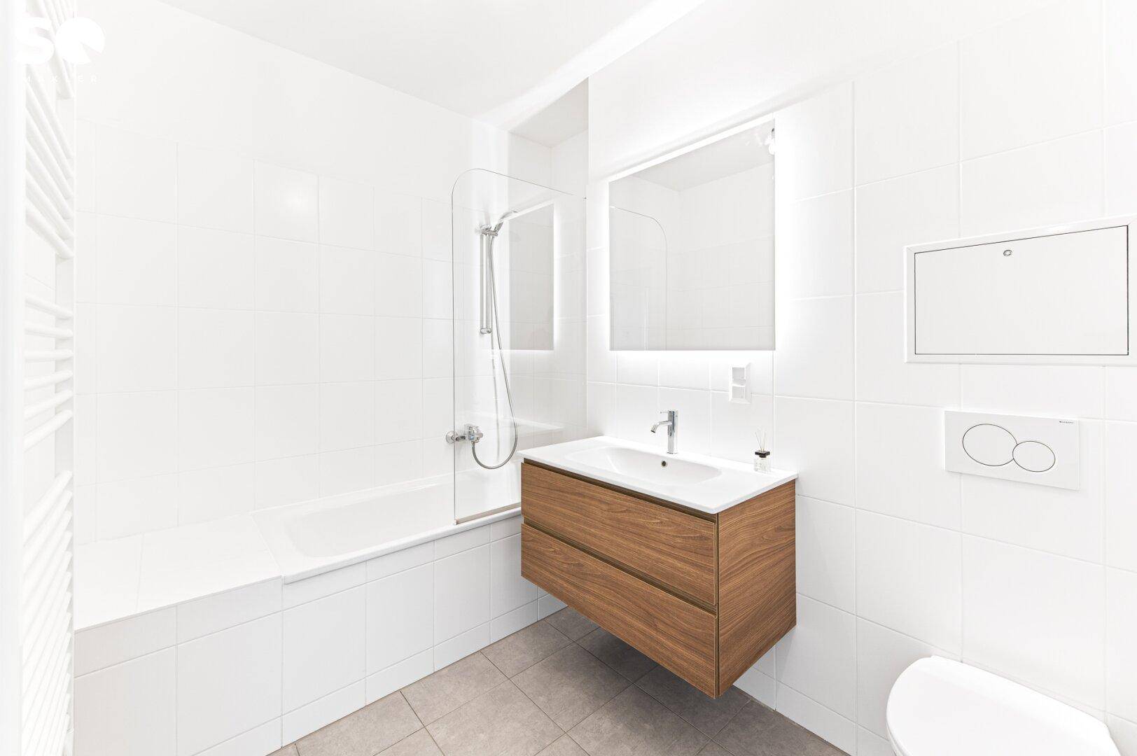 Modernes Badezimmer mit weißen Fliesen, schwebendem Waschtisch, Badewanne mit Duschwand und WC.