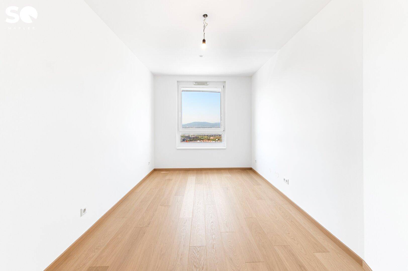 Helles Zimmer mit Holzboden und Fenster, das einen weiten Blick über die Stadt bietet.