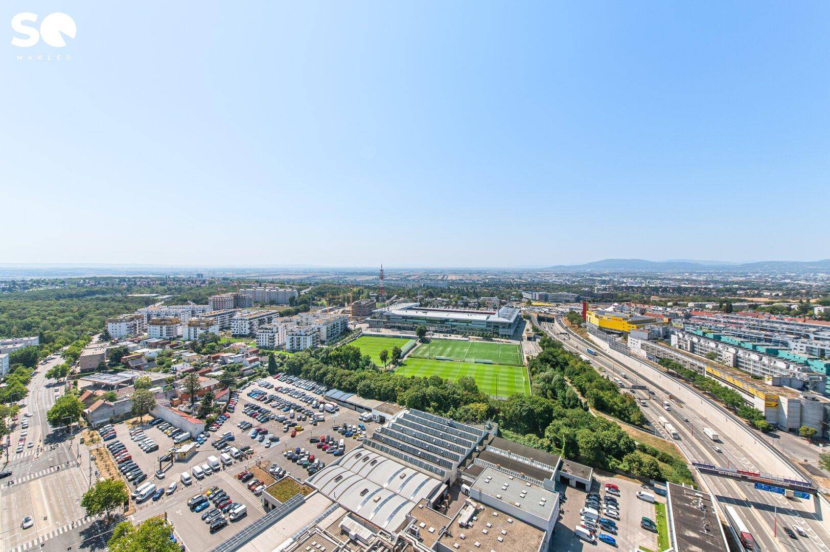 Panoramablick über die Stadt mit einem Stadion, Wohngebäuden und weitläufigen Parkplätzen.