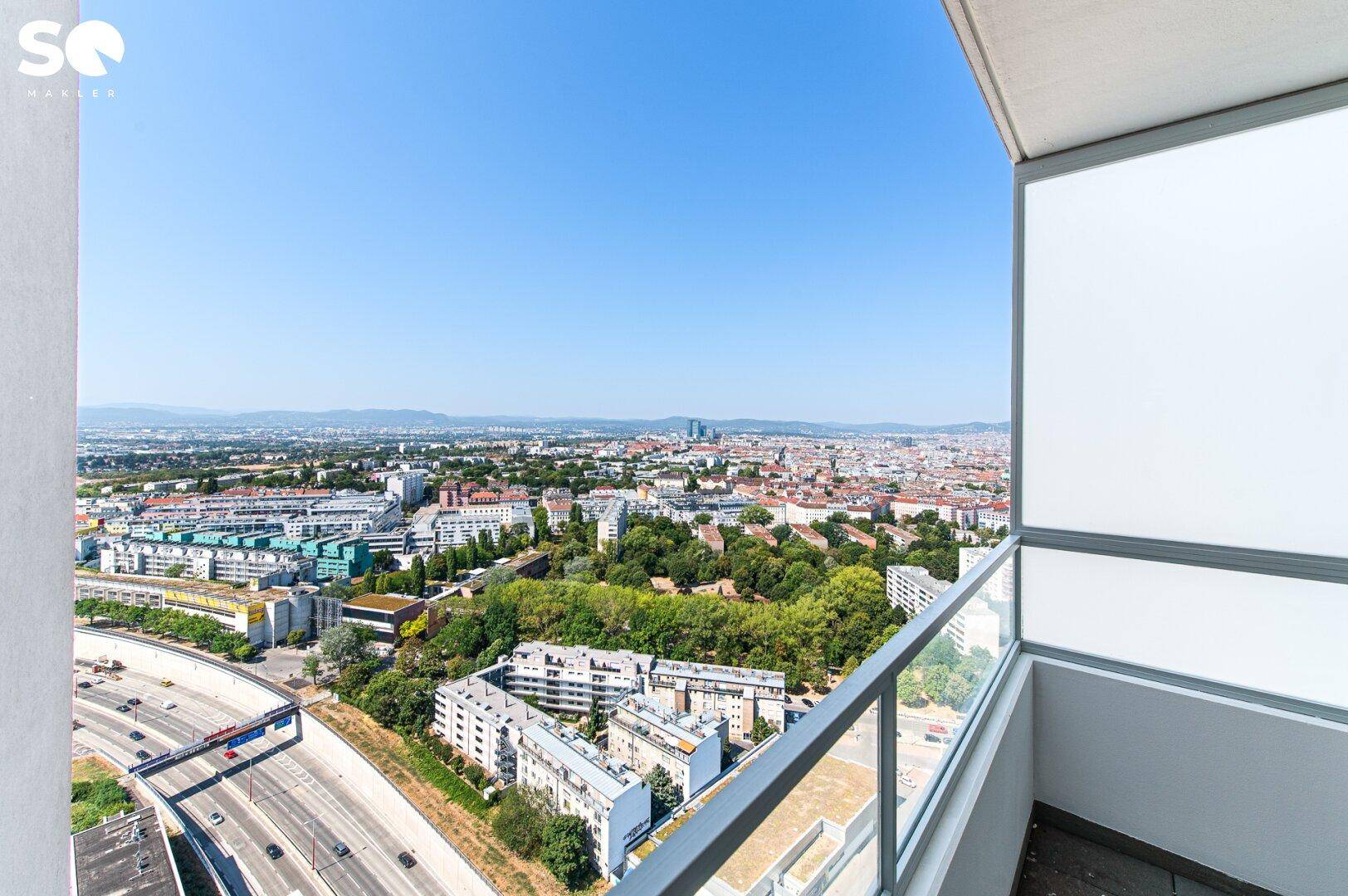 Balkon mit Glasbrüstung und weitem Blick über die Stadt und Autobahn.