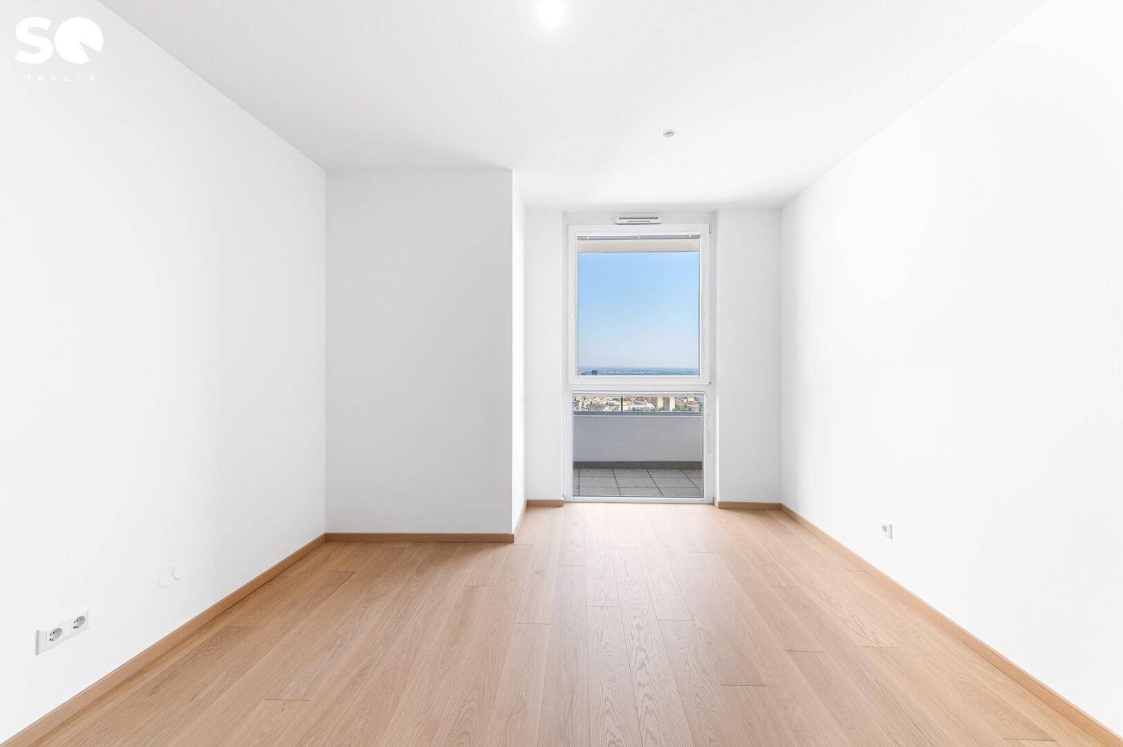 Helles Schlafzimmer mit Parkettboden und Zugang zu einem kleinen Balkon.