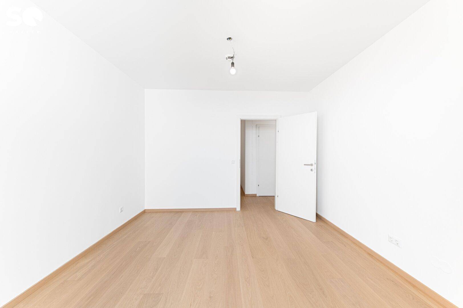 Leeres, helles Zimmer mit Parkettboden und weiß gestrichenen Wänden.