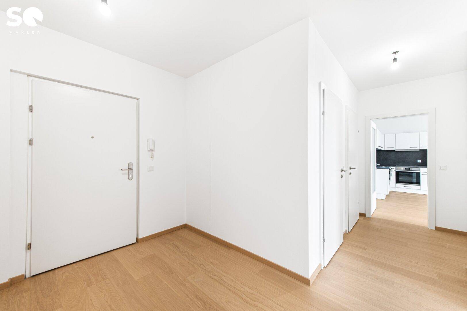 Heller Eingangsbereich mit Holzboden und weißer Tür, führt in die Wohnung.