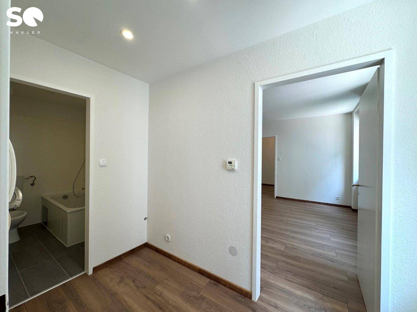Flur mit Laminatboden und Zugang zu einem Badezimmer sowie einem weiteren Wohnraum.