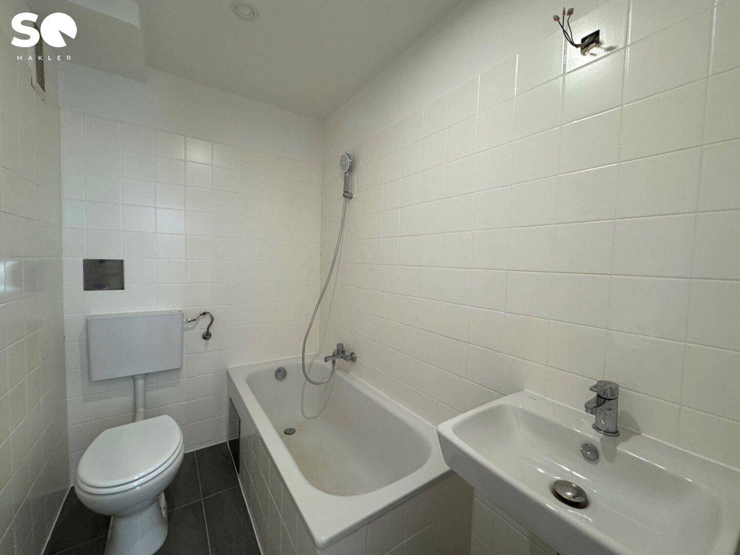 Funktionales Badezimmer mit weißen Fliesen, Badewanne, Toilette und Waschbecken.