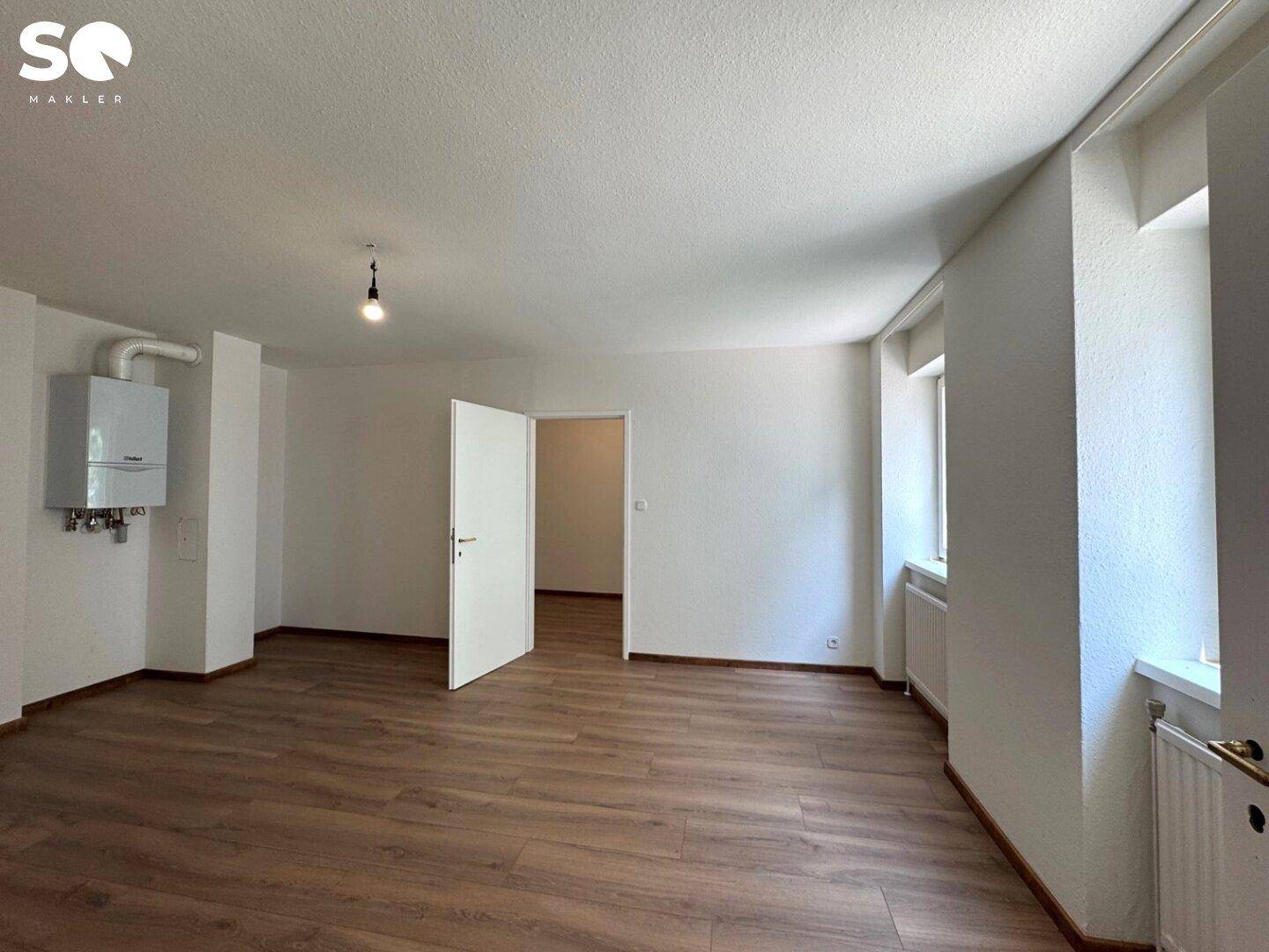Geräumiger, heller Raum mit Laminatboden, Heizkessel und Zugang zu einem angrenzenden Zimmer.
