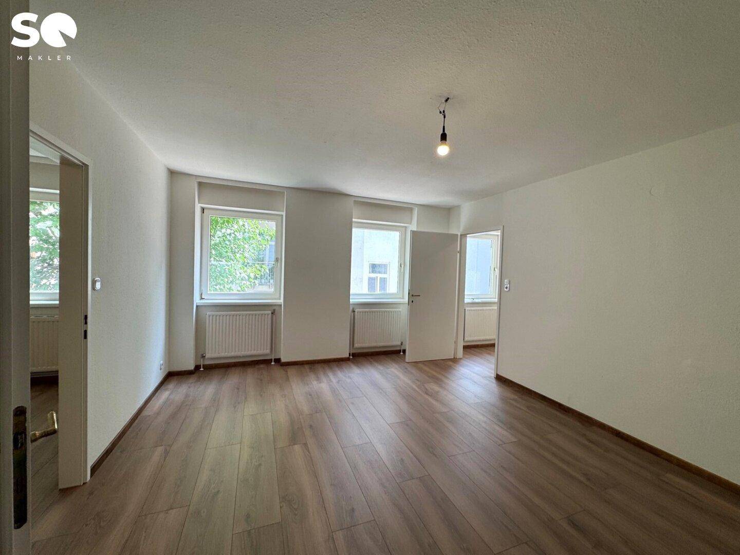 Heller, leerer Raum mit modernem Laminatboden und mehreren Fenstern für viel Tageslicht.