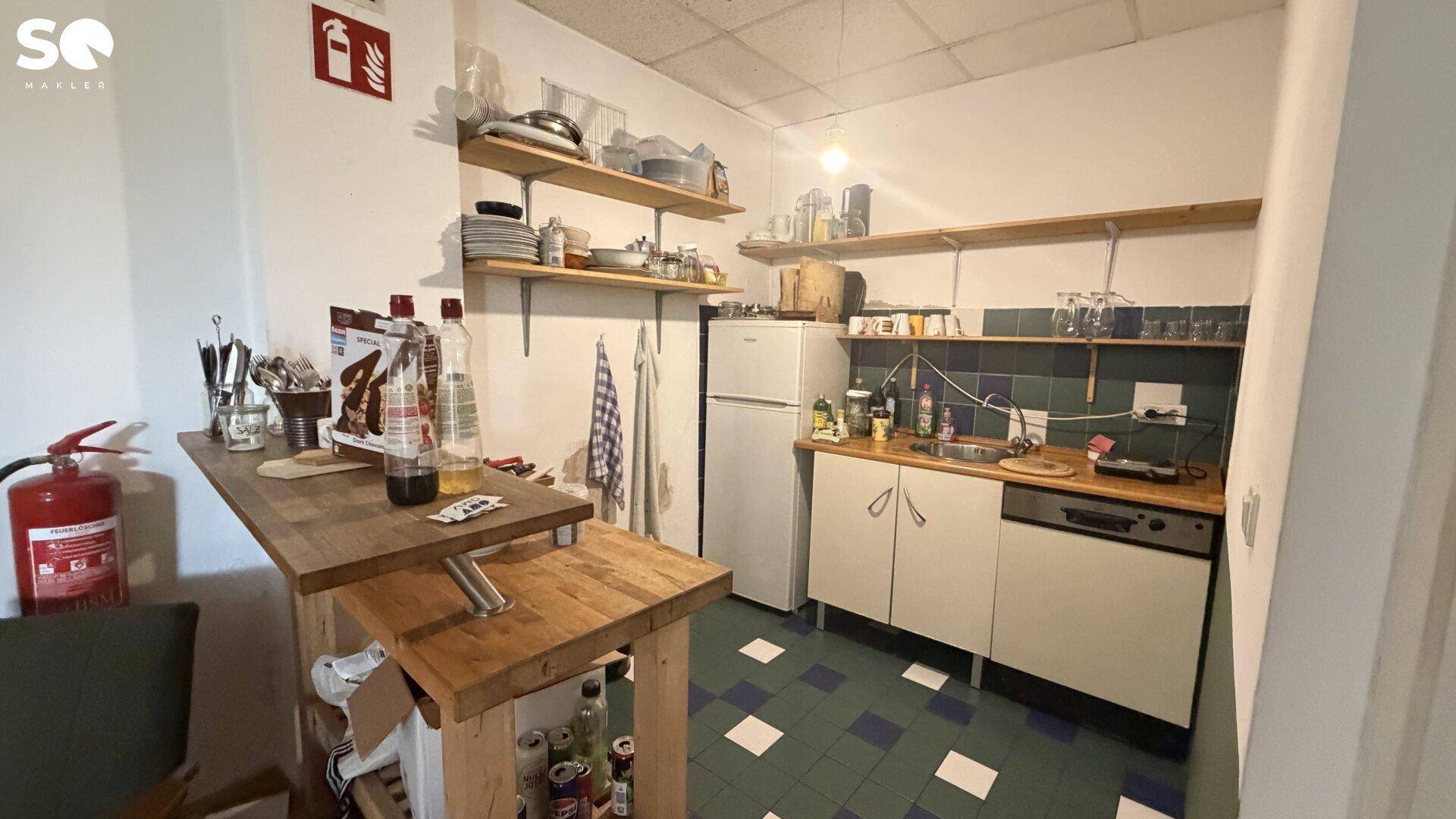 Kleine Küche mit blauen und weißen Fliesen, einem Kühlschrank und offenen Regalen für Geschirr.