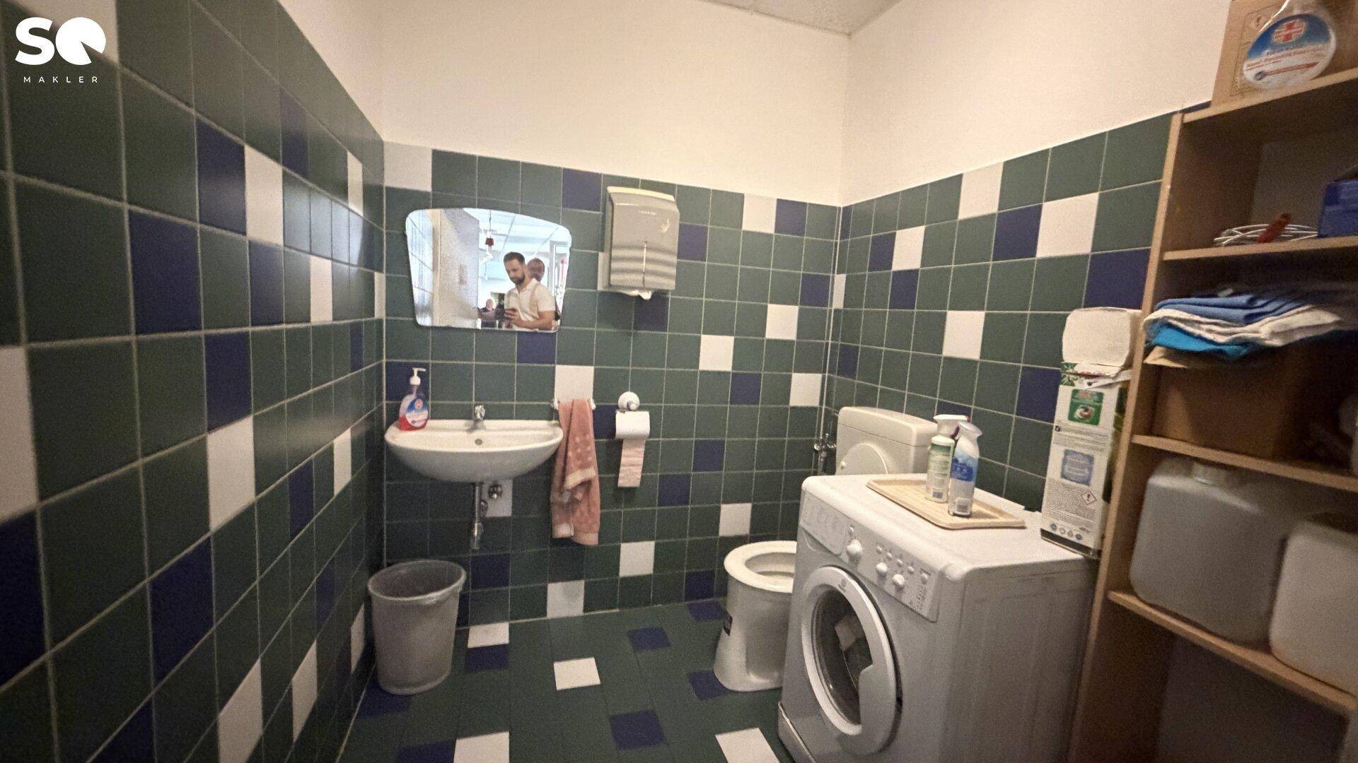 Badezimmer mit Waschbecken, Toilette und Waschmaschine, gefliest in Blau und Weiß.