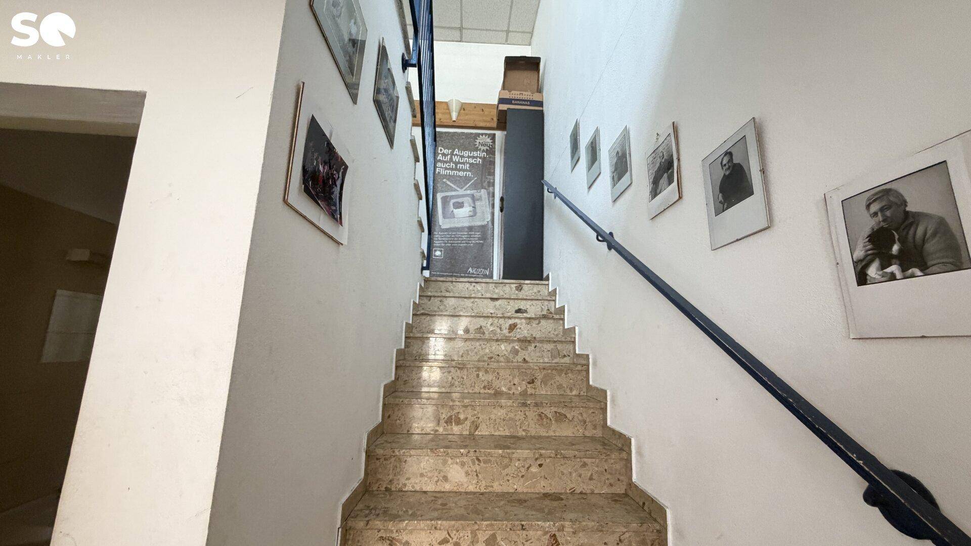 Treppenhaus mit Marmorstufen und einem schwarzen Handlauf, geschmückt mit gerahmten Bildern.