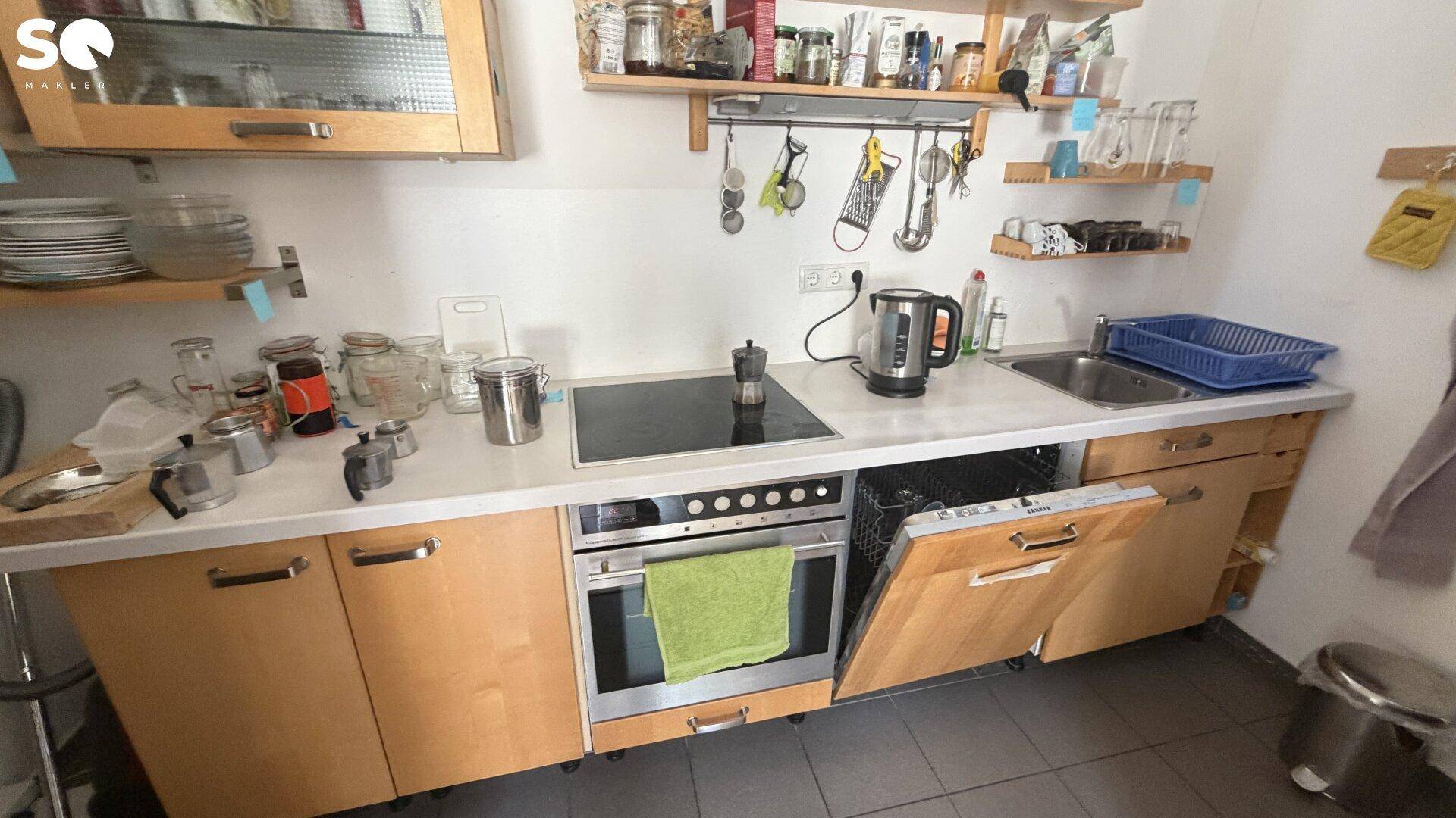 Moderne Küche mit Holzelementen, Induktionskochfeld, Backofen und integriertem Geschirrspüler.