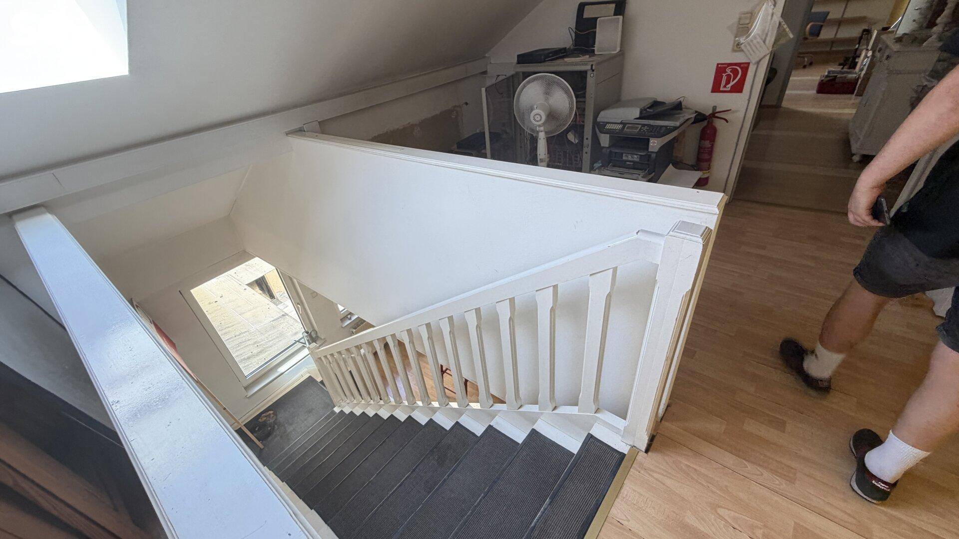 Helle Holztreppe führt in ein Obergeschoss, mit Blick auf einen weiteren Raum.