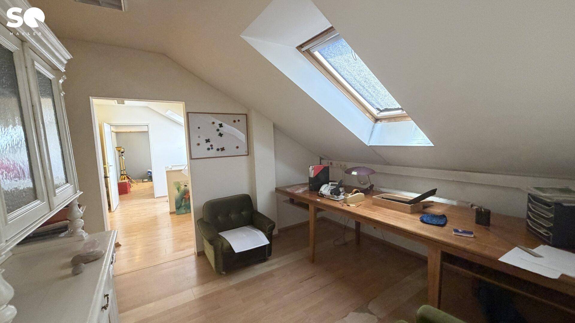 Dachgeschossbüro mit Holzboden, Dachfenster und einem langen Schreibtisch unter der Schräge.