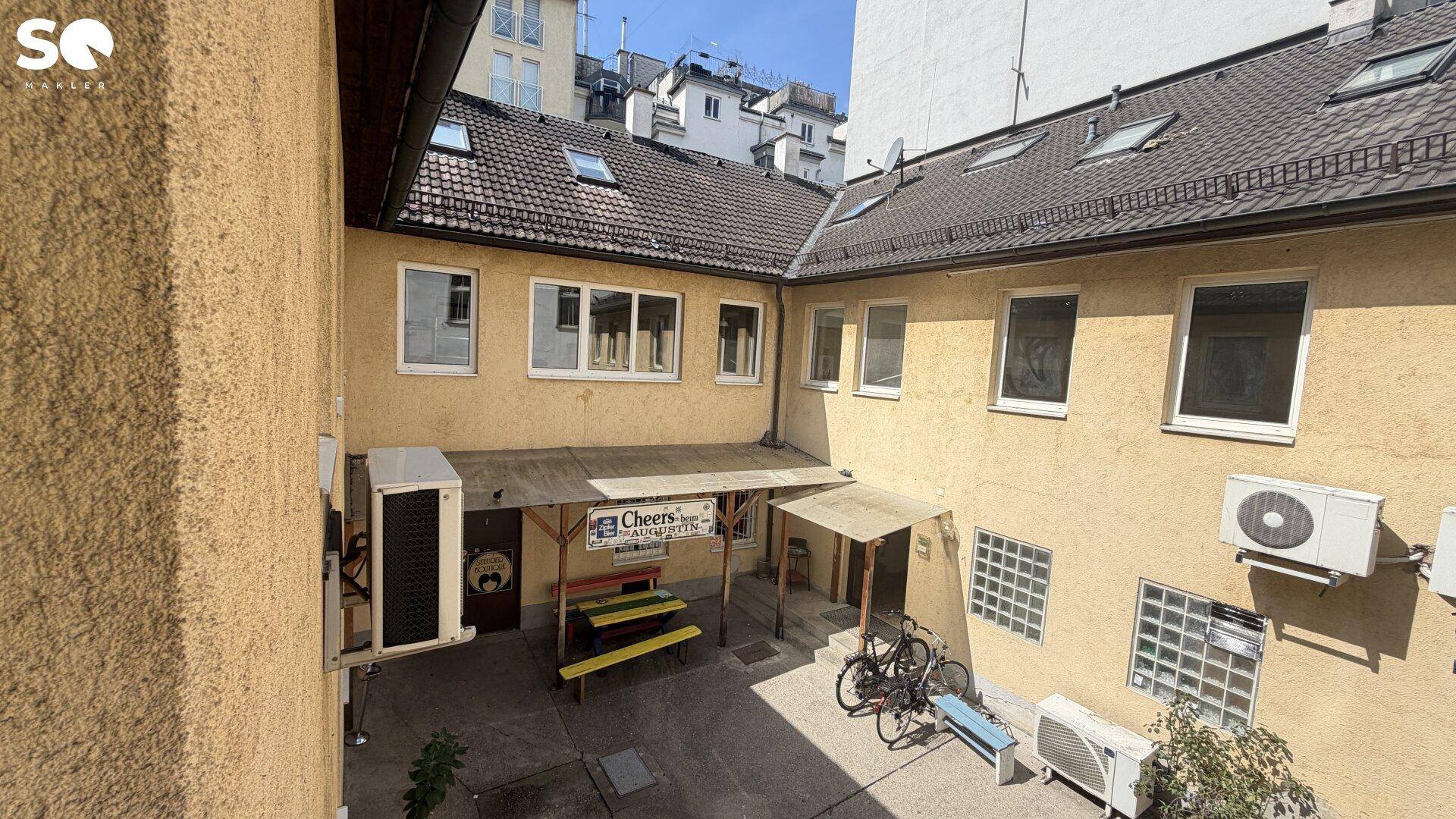 Innenhof eines Gebäudes mit mehreren Fenstern, Klimaanlagen und einem überdachten Eingangsbereich.