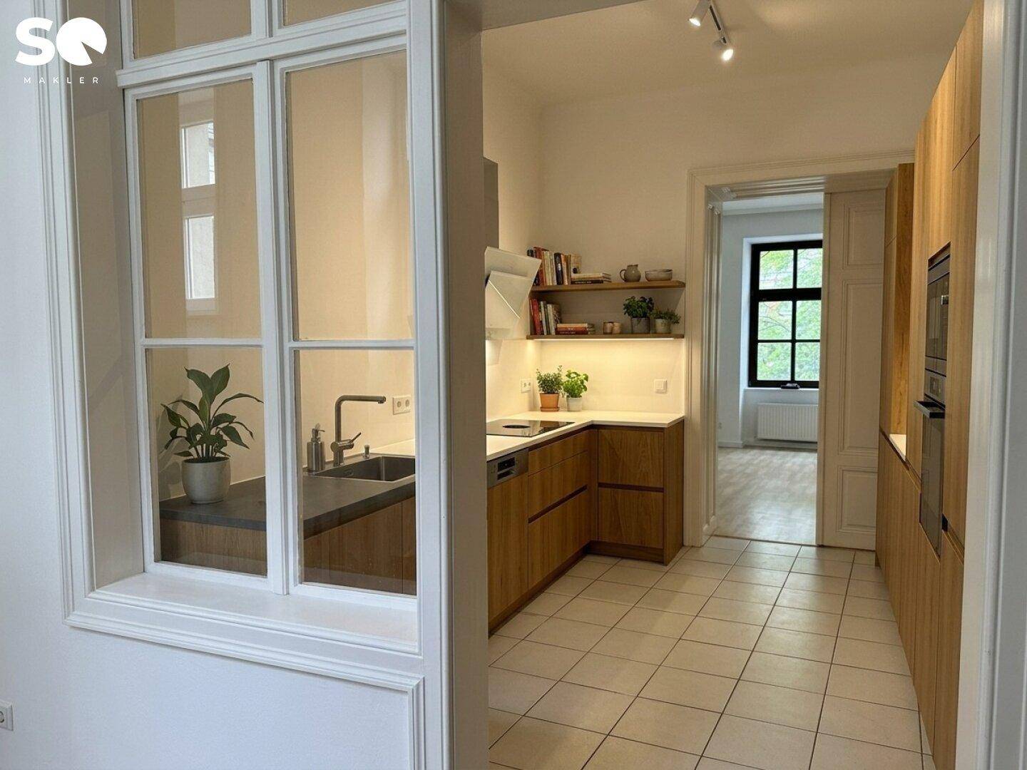 Moderne Küche mit Holzfronten, weißen Arbeitsplatten und Blick in einen angrenzenden Raum.