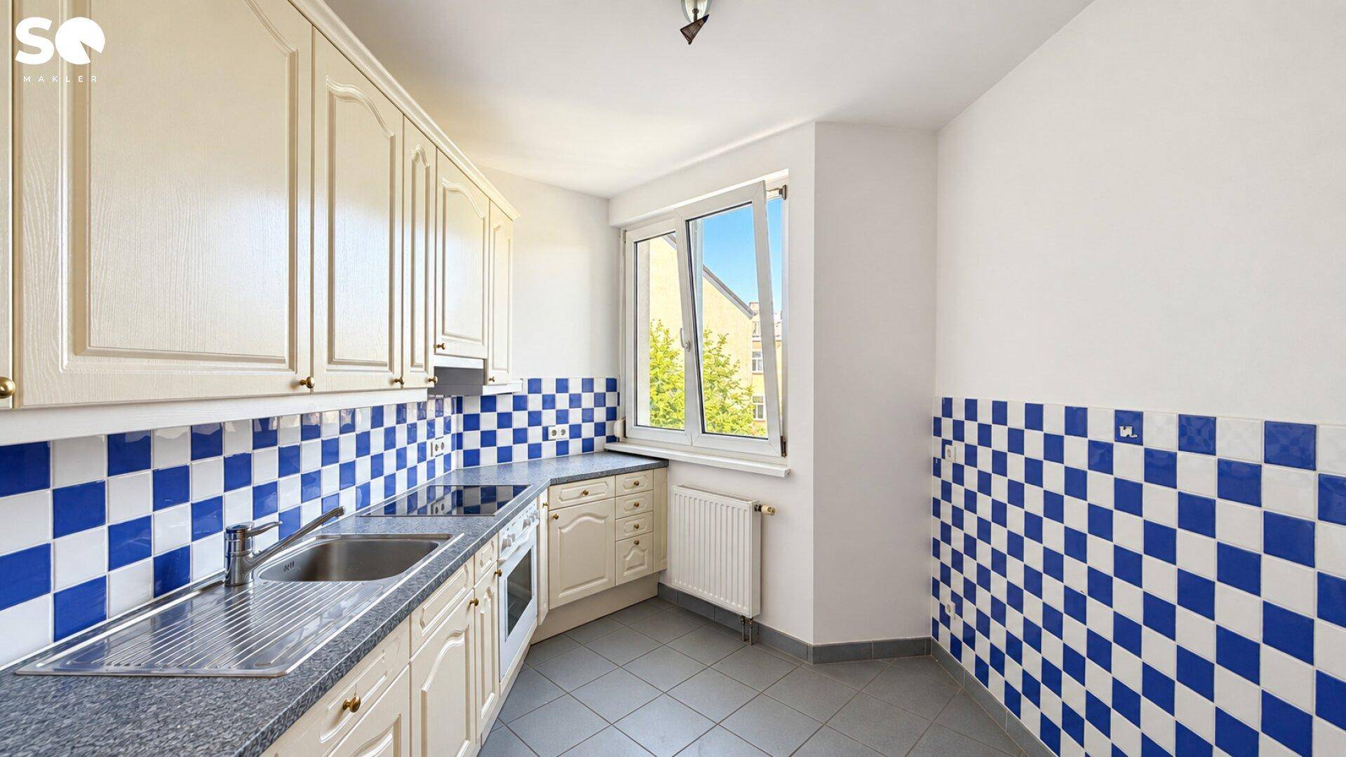 Küche mit traditionellen cremefarbenen Schränken, blauen Fliesen und Fenster.