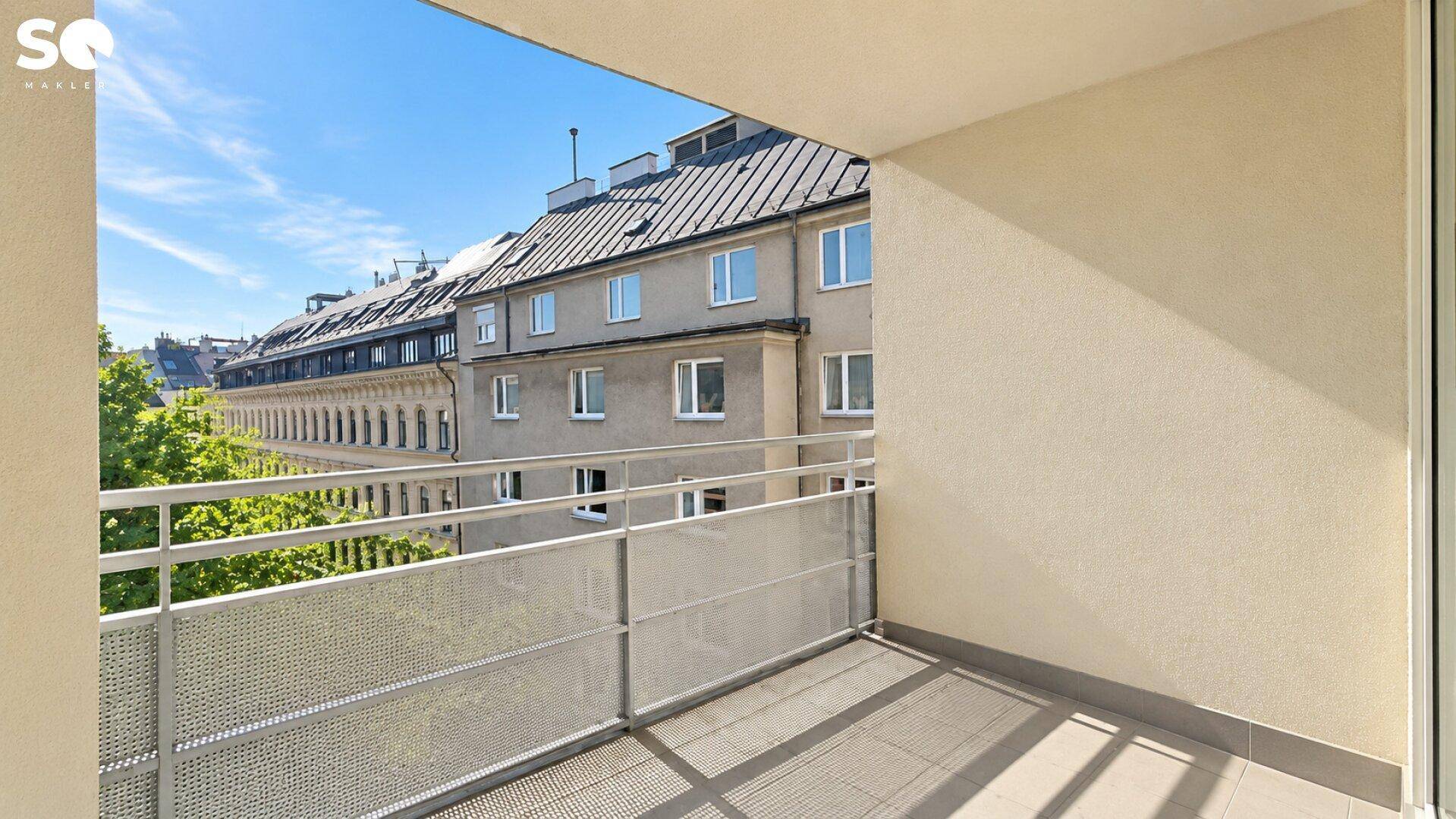 Balkon mit Metallgeländer und Blick auf die umliegenden Gebäude und Bäume.