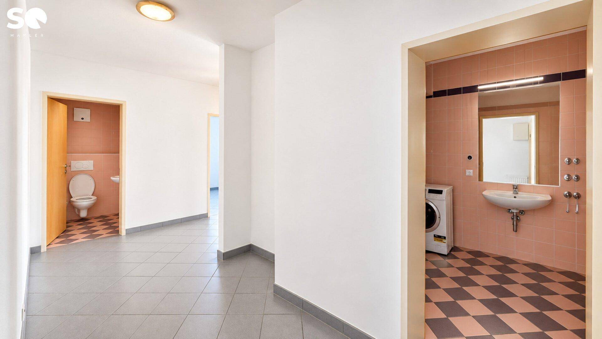 Flur mit Fliesenboden und Blick auf das Badezimmer und die separate Toilette.