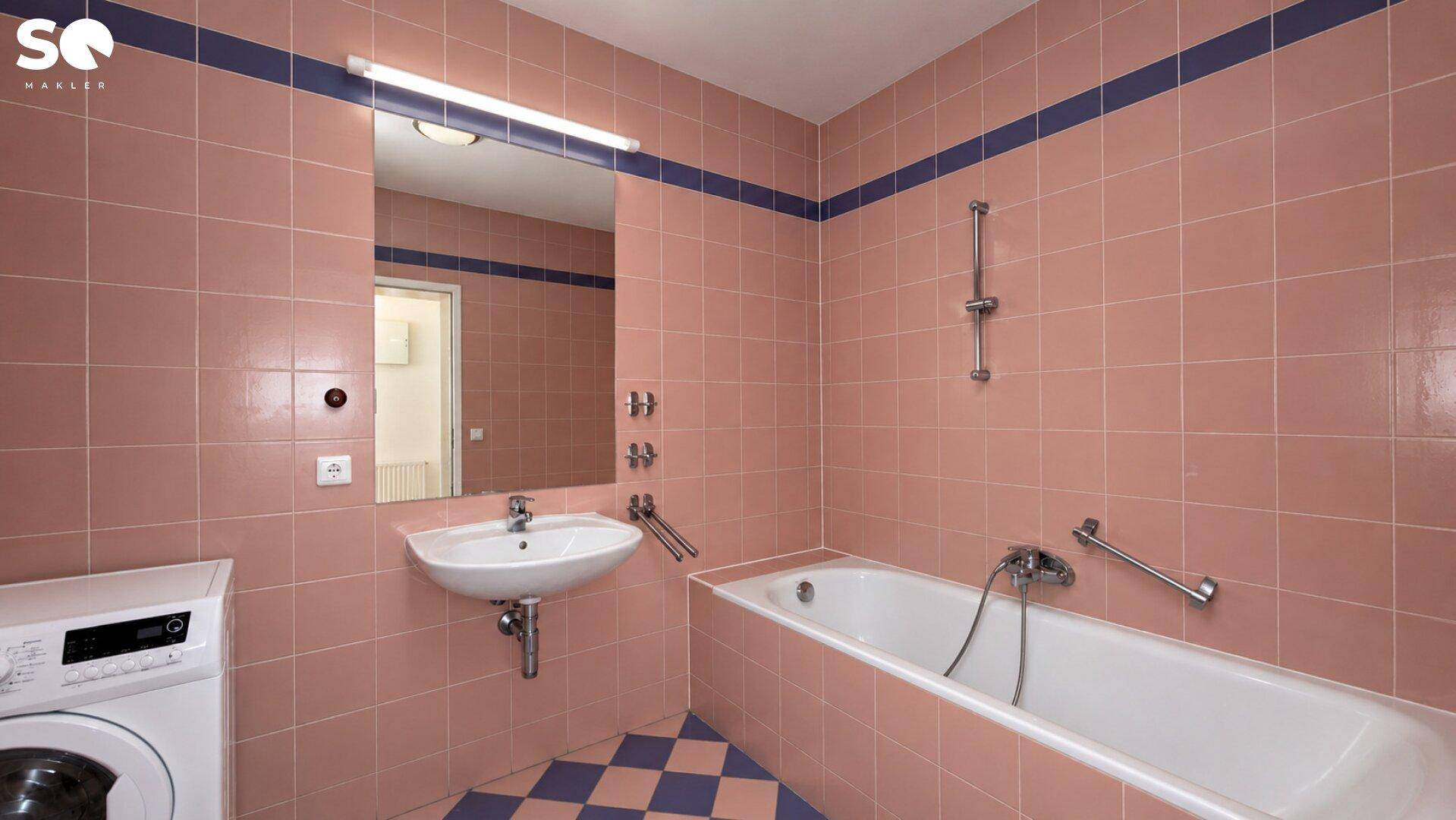 Badezimmer mit rosa Fliesen, Badewanne, Waschbecken und Waschmaschine.