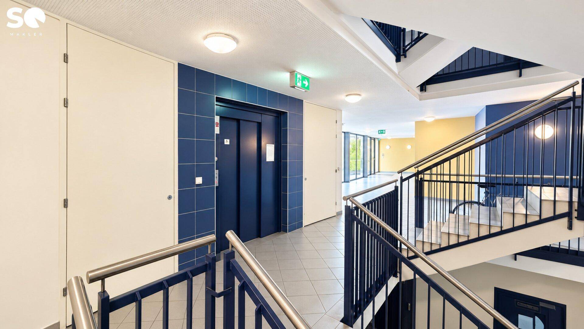Helles Treppenhaus mit Aufzug und Treppe, die zu den oberen Etagen führt.
