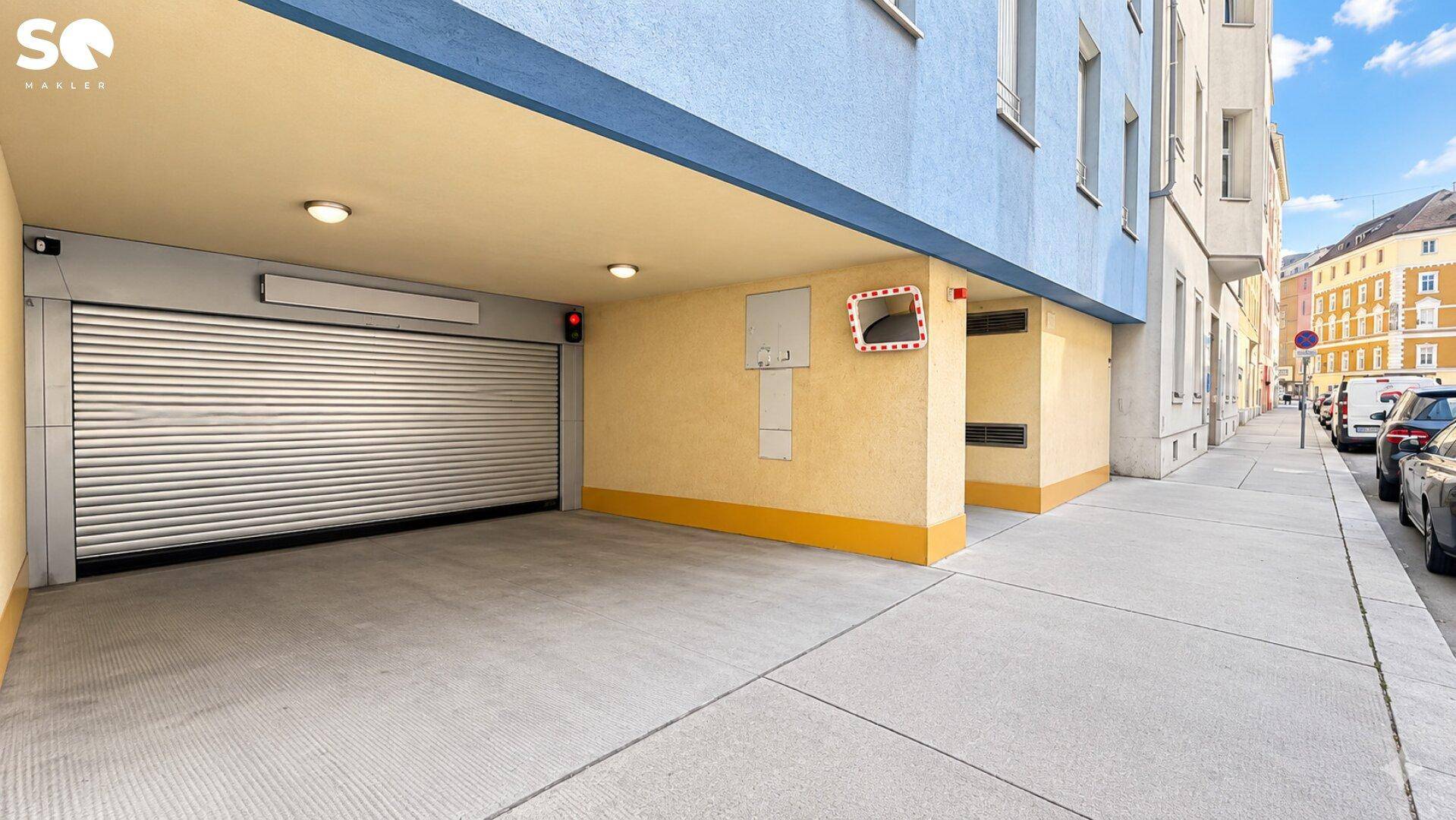 Einfahrt zu einer Tiefgarage mit Rolltor und angrenzendem Bürgersteig.