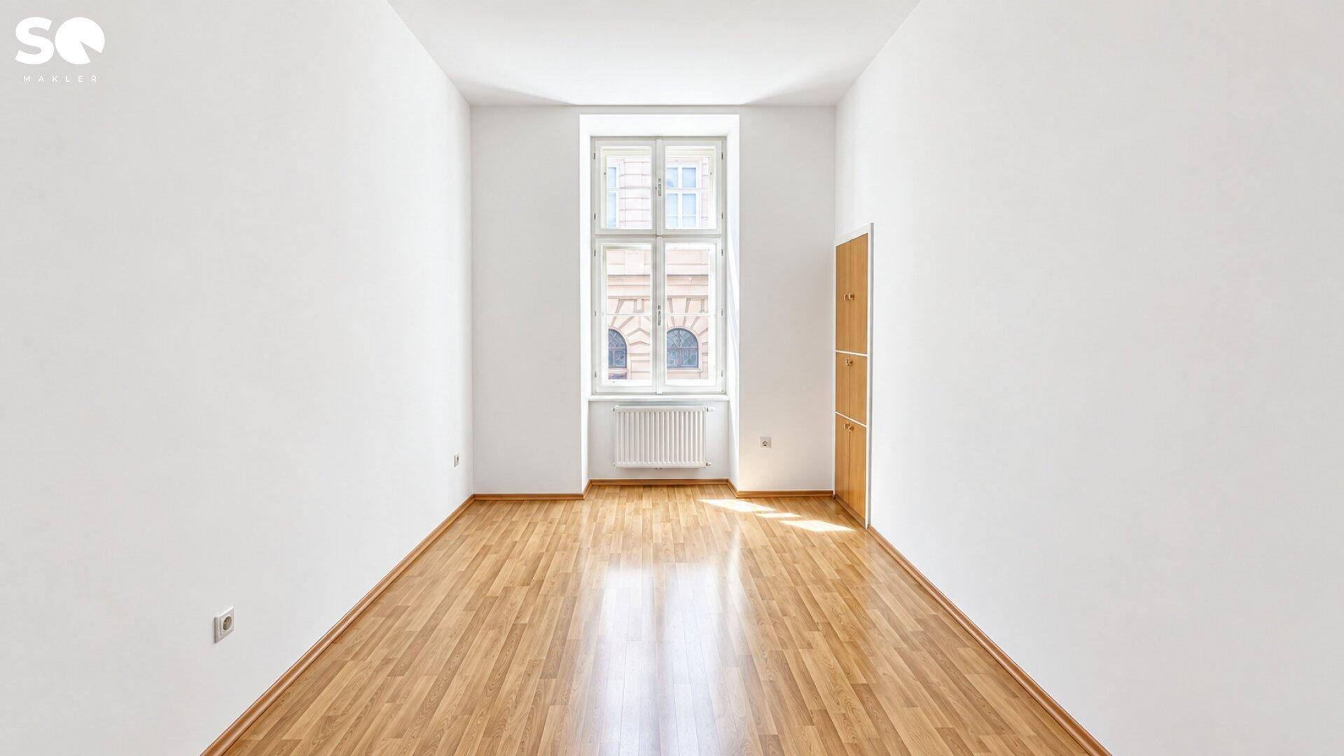 Helles, leeres Zimmer mit Holzboden und einem großen Fenster, bereit zur individuellen Gestaltung.