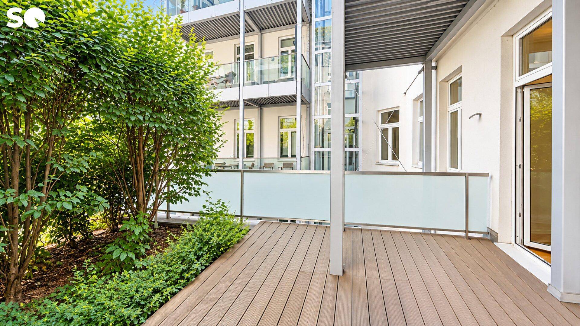 Attraktive Holzterrasse mit üppiger Bepflanzung und Blick auf die umliegenden Balkone und den Aufzug.